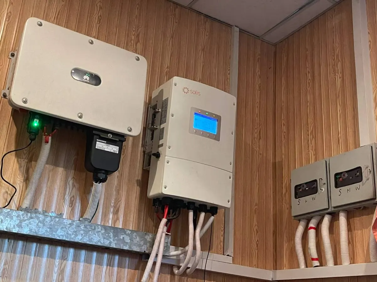 Two inverters side by side above a row of switchgear on a panelled wall