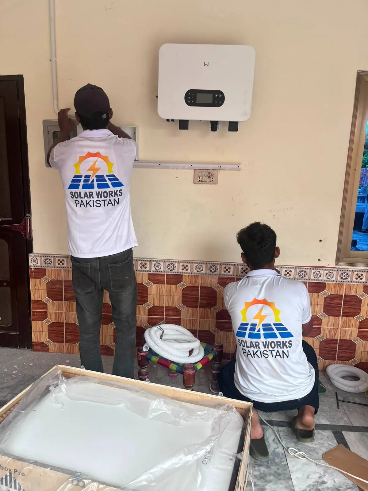 Two Solar Works Pakistan technicians in branded shirts installing an inverter